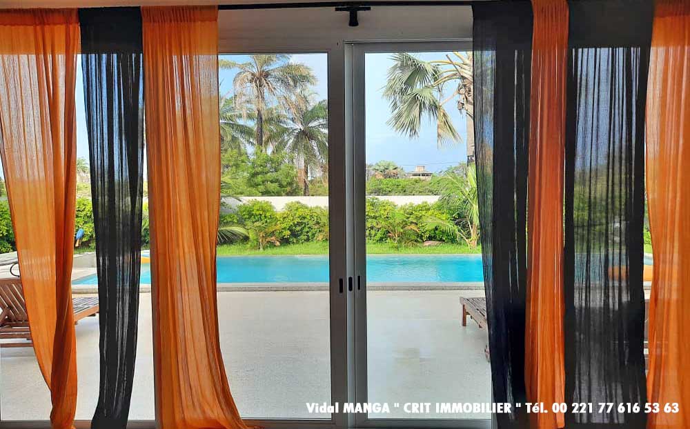 Grande baie vitrée avec vue sur la piscine et  jardins de la villa maison construite en deuxième ligne tout proche de la plage et des commerces